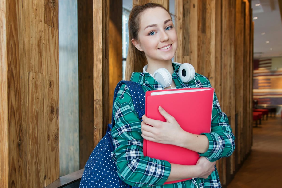 A smiling student with a book and bag